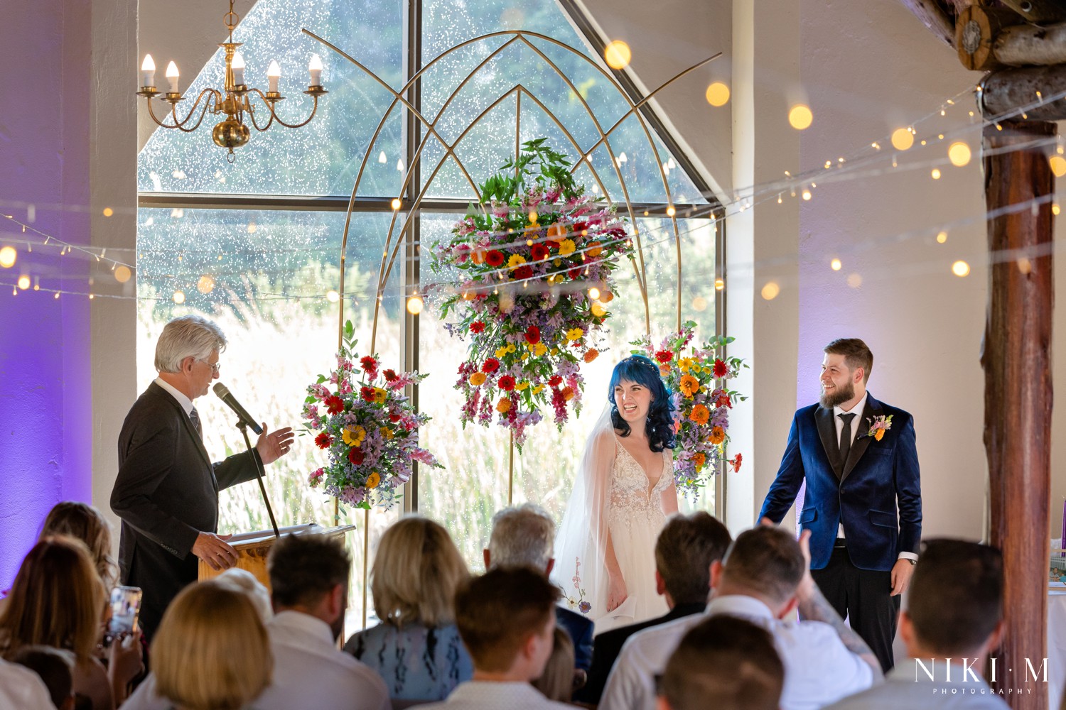 Wide ceremony shot with a gold floral arch and the Drakensberg mountains through the window, photographed by Drakensberg wedding photographer