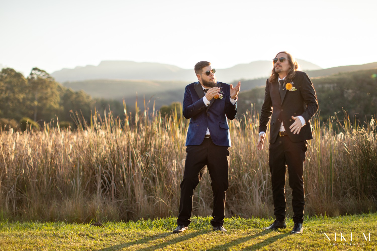 Groom and groomsman laughing in golden hour grasslands at a Champagne Valley Drakensberg wedding