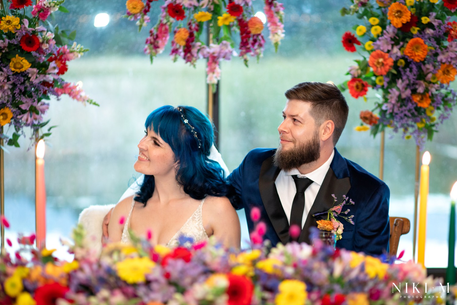 Bride and groom at their sweetheart table surrounded by wildflowers and a gold floral arch at a Drakensberg wedding reception