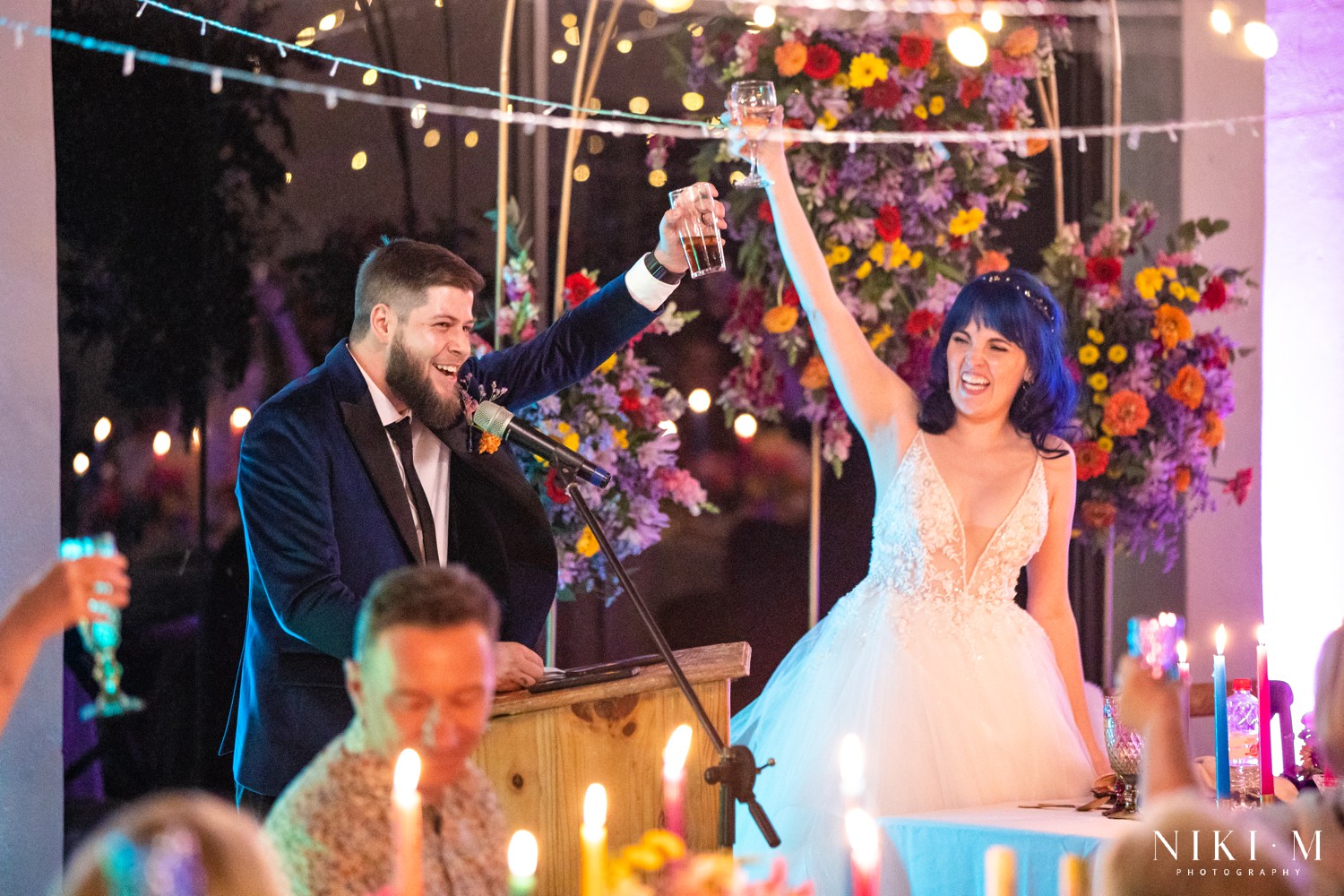 Bride and groom raising their glasses together in a toast with fairy lights above at a Drakensberg wedding