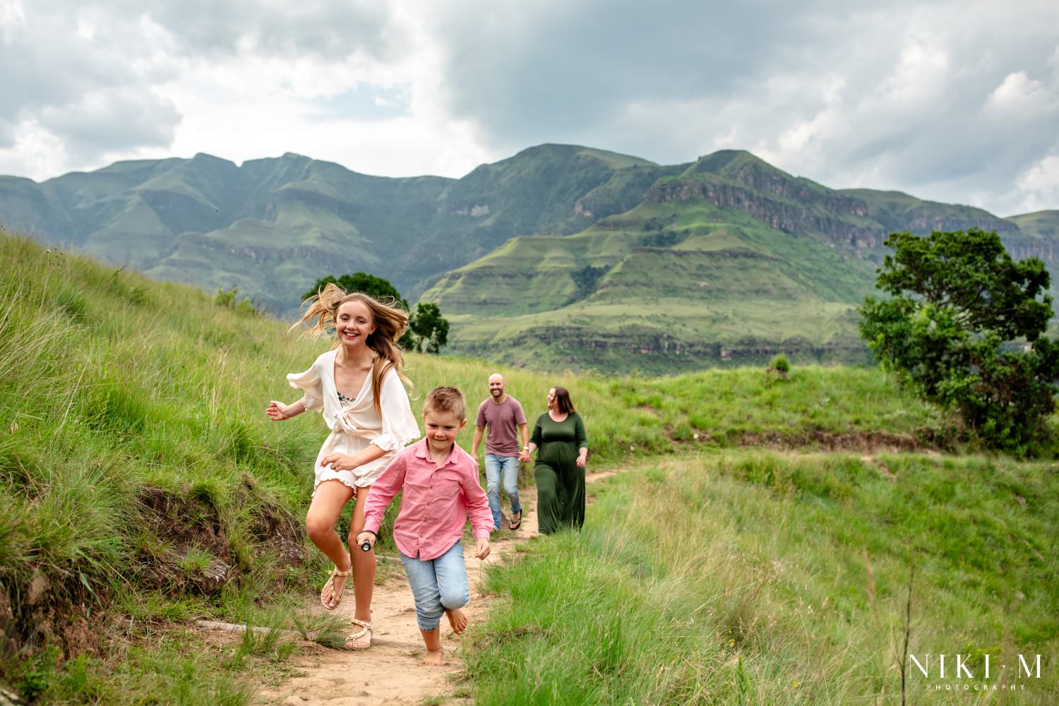 Children running barefoot down the Monks Cowl trail with parents walking behind in the Central Drakensberg