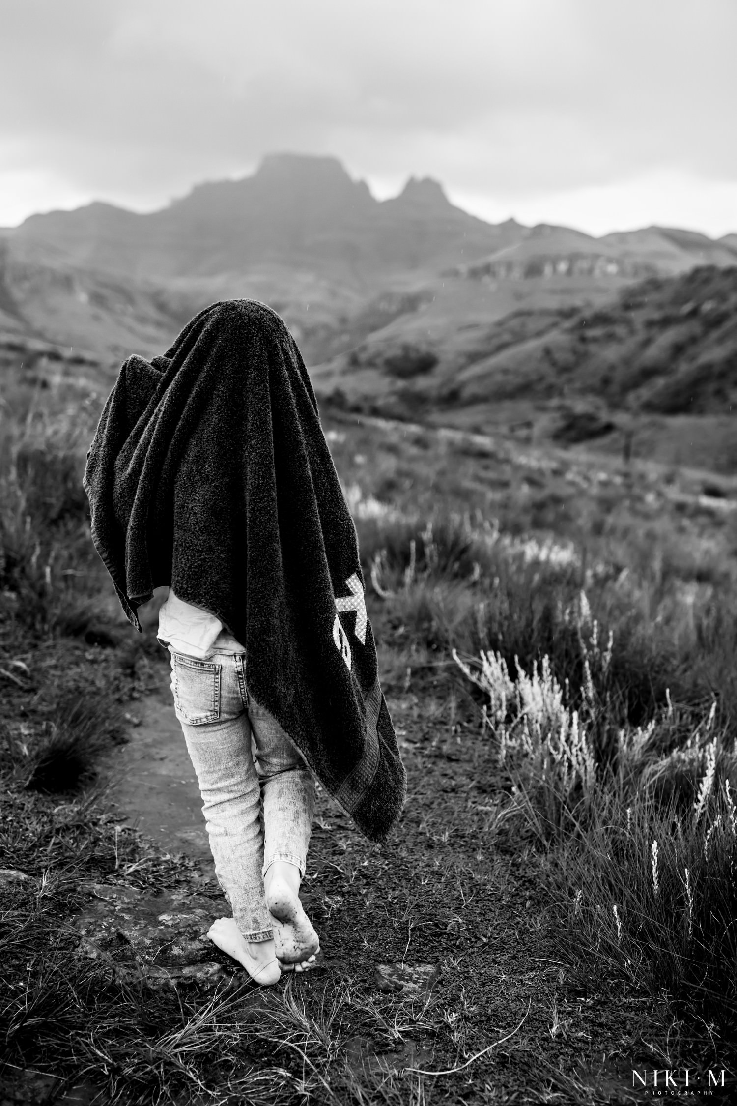 Black and white image of a child wrapped in a towel walking the Monks Cowl trail during a Drakensberg thunderstorm