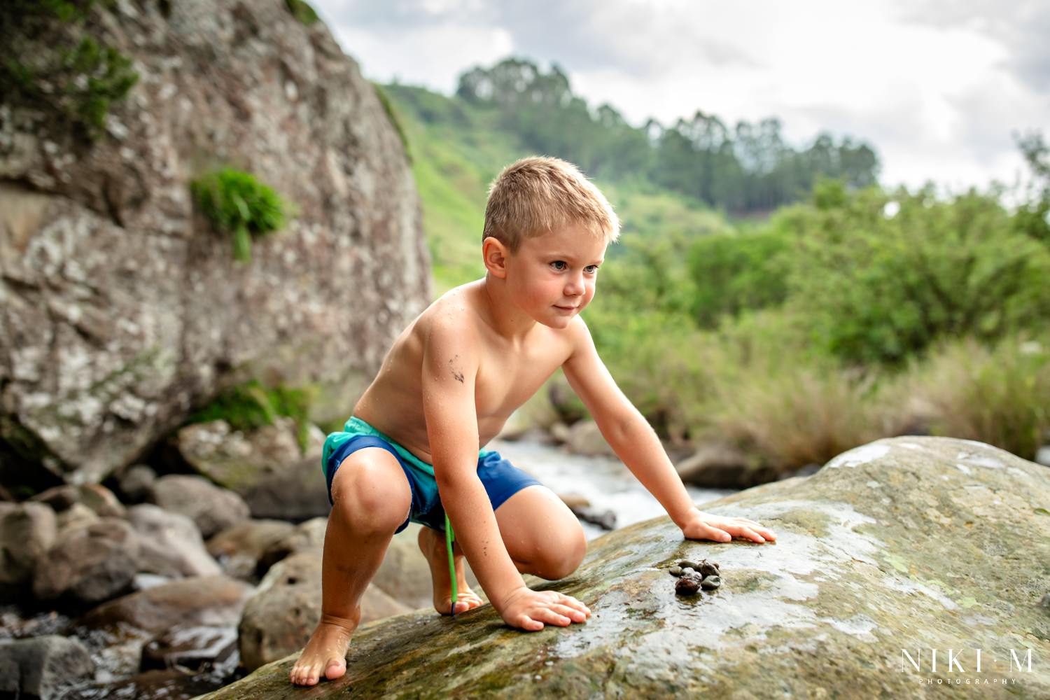 Young boy crouching on a boulder beside the stream at Monks Cowl Reserve, Central Drakensberg